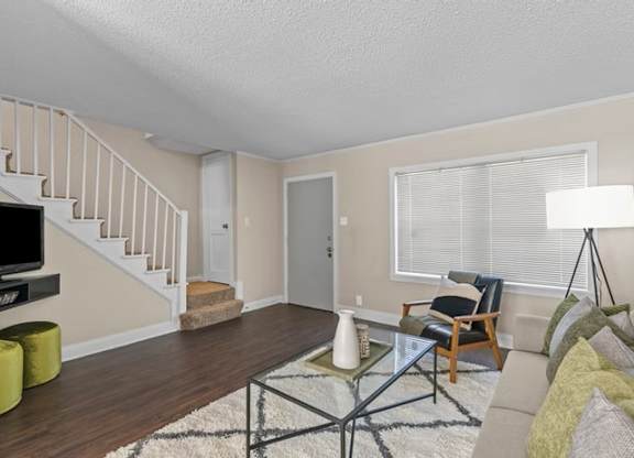A living room with a staircase and a glass coffee table.