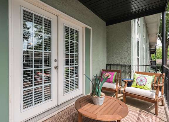A patio with a table, two chairs and a potted plant.