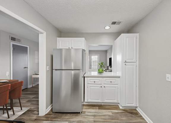 A kitchen with a refrigerator, cabinets, and a dining table.