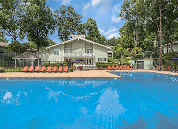 A swimming pool in front of a house with orange lounge chairs.