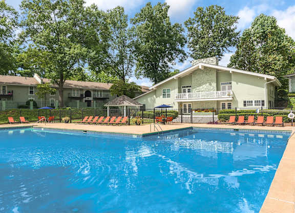 A swimming pool in front of a house with trees in the background.