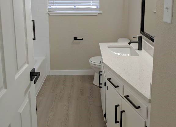 A white bathroom with a toilet, sink, and a window with blinds.