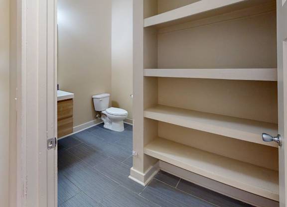 A white toilet is in a small room with a shelf.