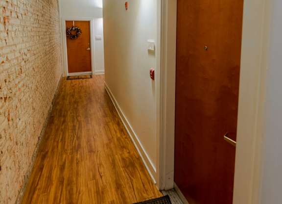 A hallway with a brick wall on the left and a wooden door on the right.