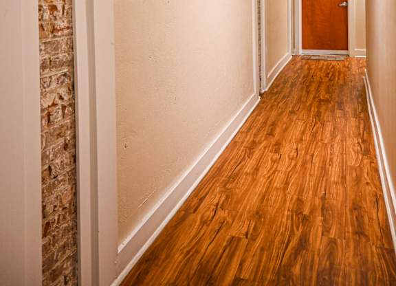 A long hallway with a brick wall on the left and a wooden door on the right.
