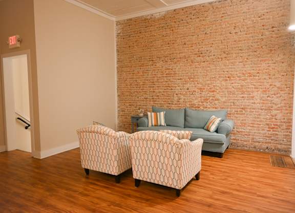 Two chairs and a couch are in a room with a brick wall.
