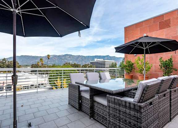 A patio with a table and chairs under umbrellas.at Catania, Pasadena, 91105