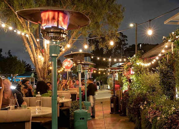 A restaurant with tables and chairs under umbrellas and string lights.at The Wilson, Santa Monica, CA