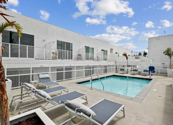 A pool area with sun loungers and a white building in the background.at The Dillon II at Silver Lake, Los Angeles