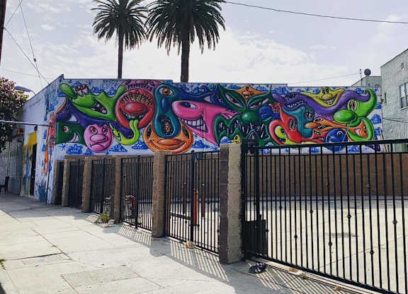 A colorful mural of a face and a dinosaur is painted on a building.at 5135 W Adams, Los Angeles California