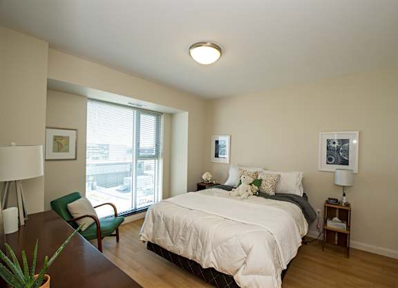A bedroom with a bed, chair, and window.