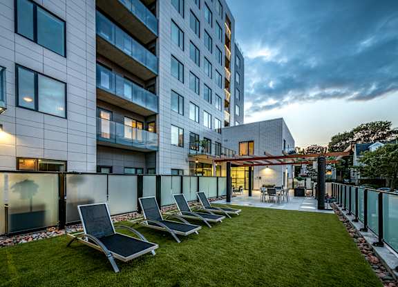 A modern building with a glass facade and a small garden area with lounge chairs.