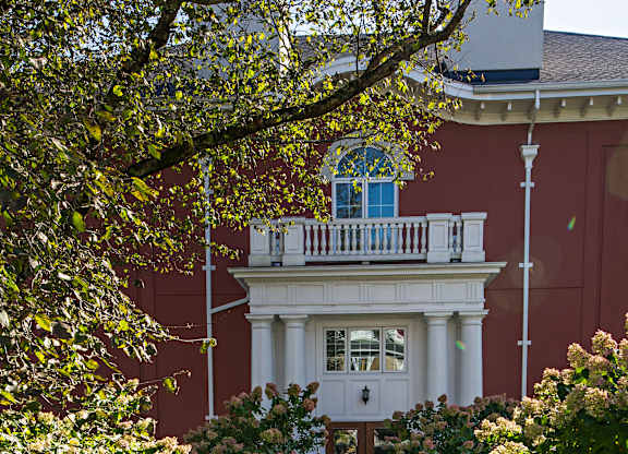A white building with a balcony is surrounded by green plants.