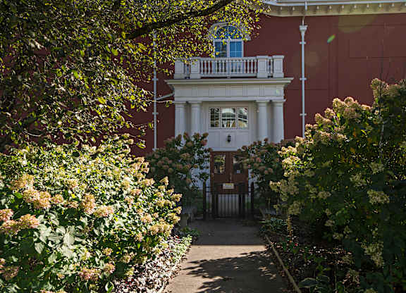 A white house with a balcony is surrounded by greenery.