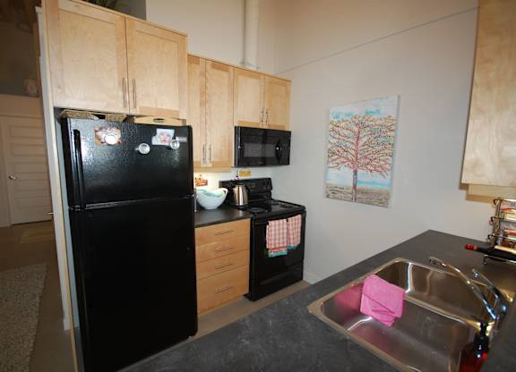 A black fridge in a kitchen with a pink towel in the sink.