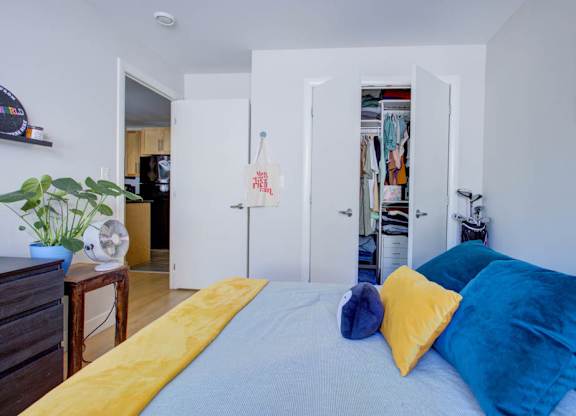 A bed with a yellow blanket and blue pillows is in the foreground of a room.