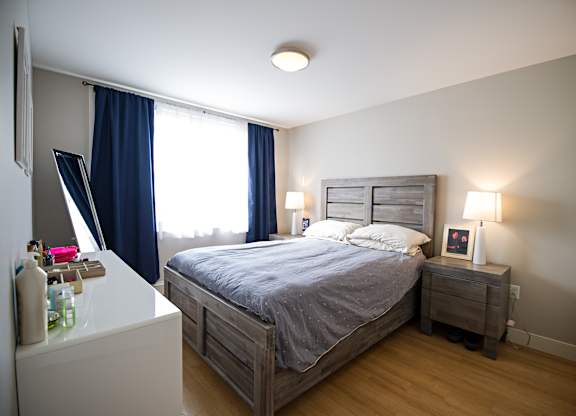 A bedroom with a bed, nightstand, and window with blue curtains.