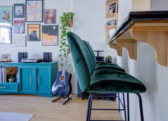 A green chair sits in front of a wooden desk with a guitar leaning against the wall.