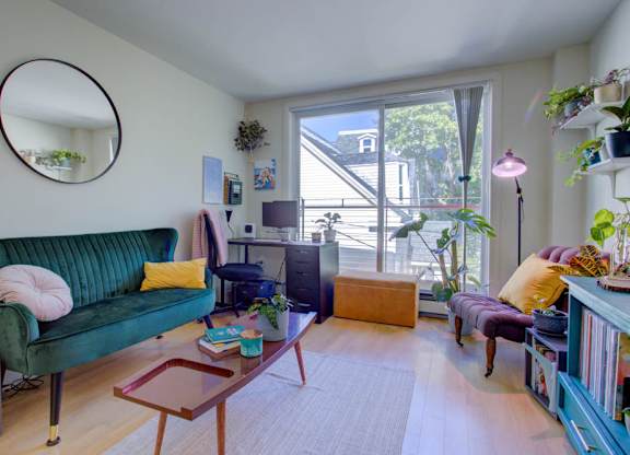 A living room with a green couch and a round mirror on the wall.