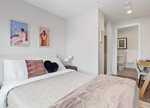 A bedroom with a bed, two pillows, a nightstand, a chair, and a painting on the wall.