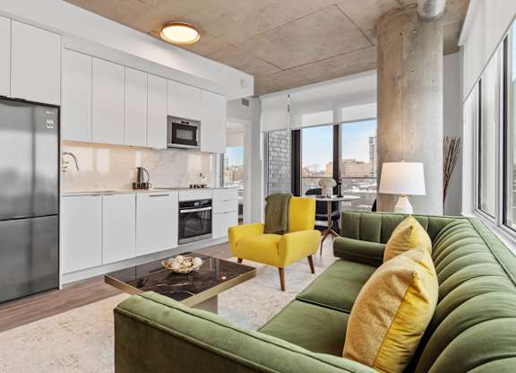 A modern kitchen with a green couch and yellow chair.