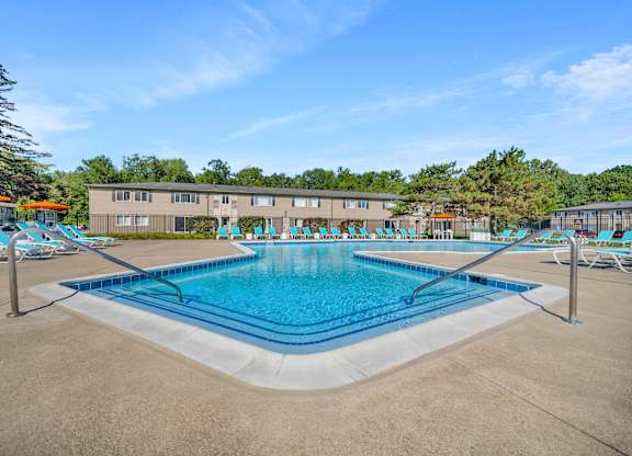 A large swimming pool with lounge chairs and a building in the background.
