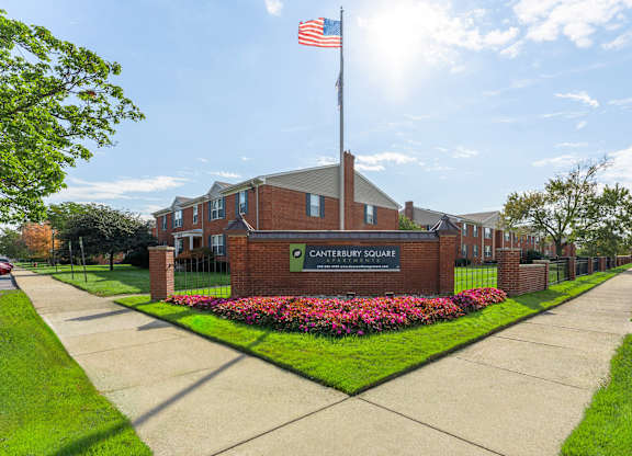 The image shows a building with the name "CANTERBURY SQUARE" on it, surrounded by a flower bed and a clear sky above.