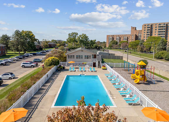 A large swimming pool surrounded by a white fence and orange umbrellas.