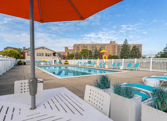 A pool area with a white table and chairs under an orange umbrella.