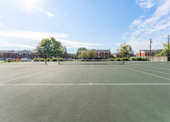 A tennis court with a clear blue sky and some clouds.