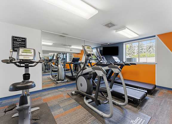 A gym with a row of treadmilers and elliptical machines.