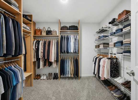 A walk-in closet with clothes and shoes organized on shelves and hangers.