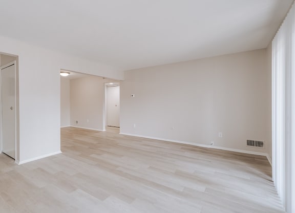 A spacious room with light wood flooring and white walls.