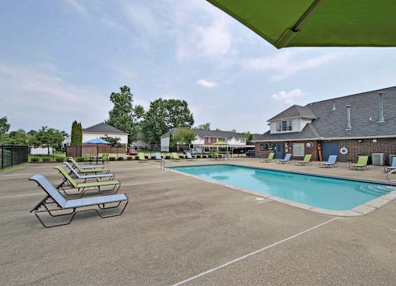 A pool area with sun loungers and a green umbrella.