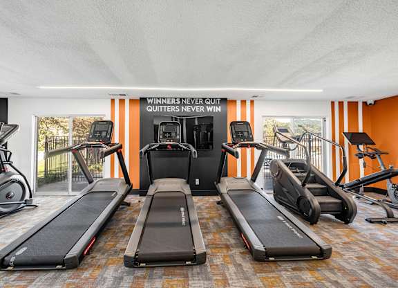 A gym with treadmills, elliptical machines, and a sign that says "Winners never quit, quitters never win.".