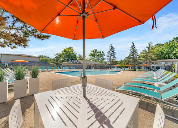A sunny day at the poolside with a bright orange umbrella providing shade.