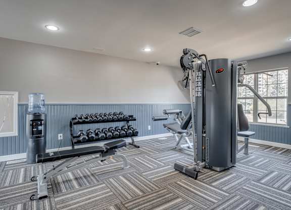A gym with a variety of equipment including a treadmill, weights, and a bench.