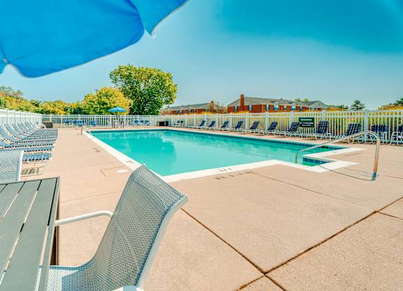 A pool with chairs and a table is surrounded by a blue umbrella.