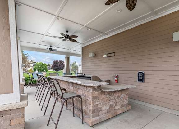 A patio with a bar and chairs under a ceiling fan.