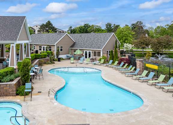A large outdoor swimming pool surrounded by lounge chairs and a building in the background.