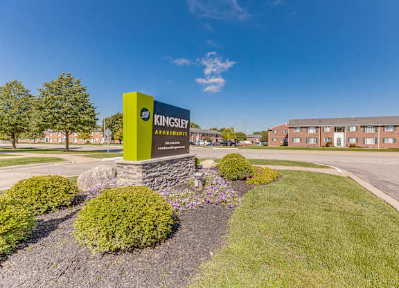 A green and yellow sign for Kingsley Apartments stands in front of a building.
