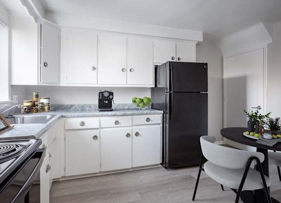 A black refrigerator stands in a kitchen with white cabinets and a marble countertop.