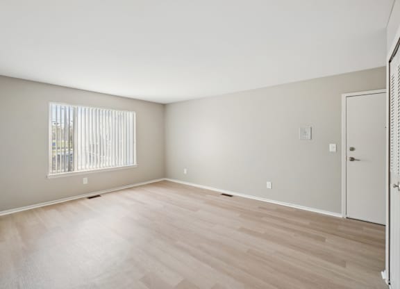 A room with wooden flooring and a window with blinds.