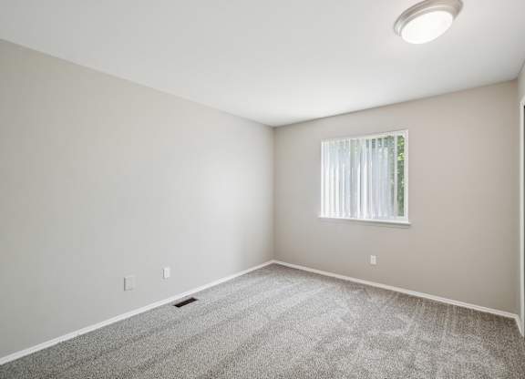 A room with a carpeted floor and a window with blinds.