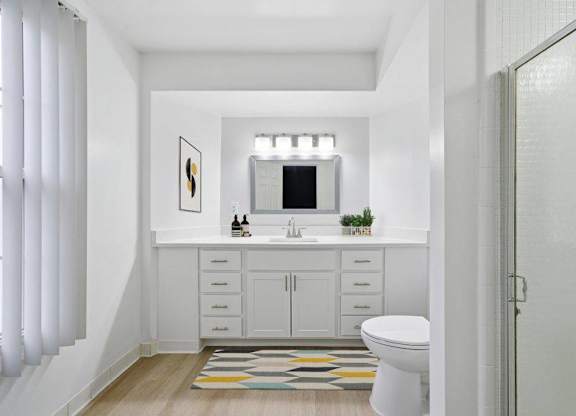 A white bathroom with a toilet, sink, and a rug on the floor.