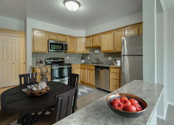 A kitchen with wooden cabinets and a black table with a bowl of apples on it.