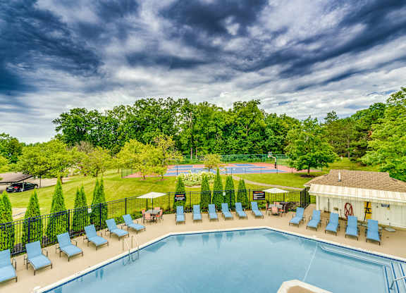 A large swimming pool surrounded by lawn chairs and trees.