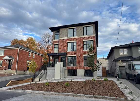 A modern two-story brick house with a black roof and a grey garage door.