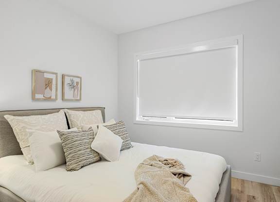 A bedroom with a bed, pillows, and pictures on the wall.