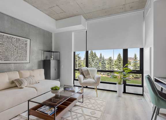 A living room with a white couch, a coffee table, and a large window with a view of trees.